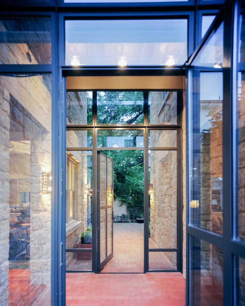 A glass and brick hallway connecting two parts of a house.