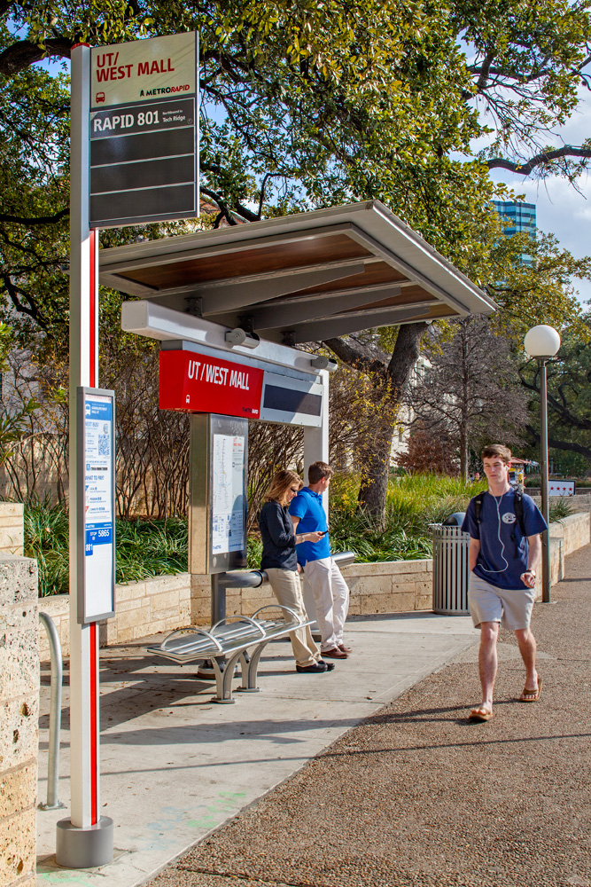 People waiting at bus stop while student walks by.