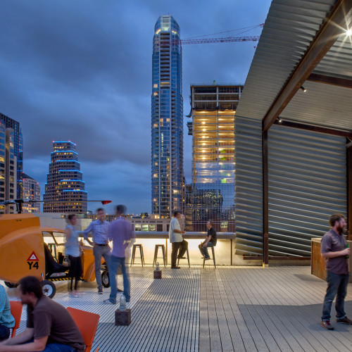 People socializing on downtown Austin rooftop deck at dusk.
