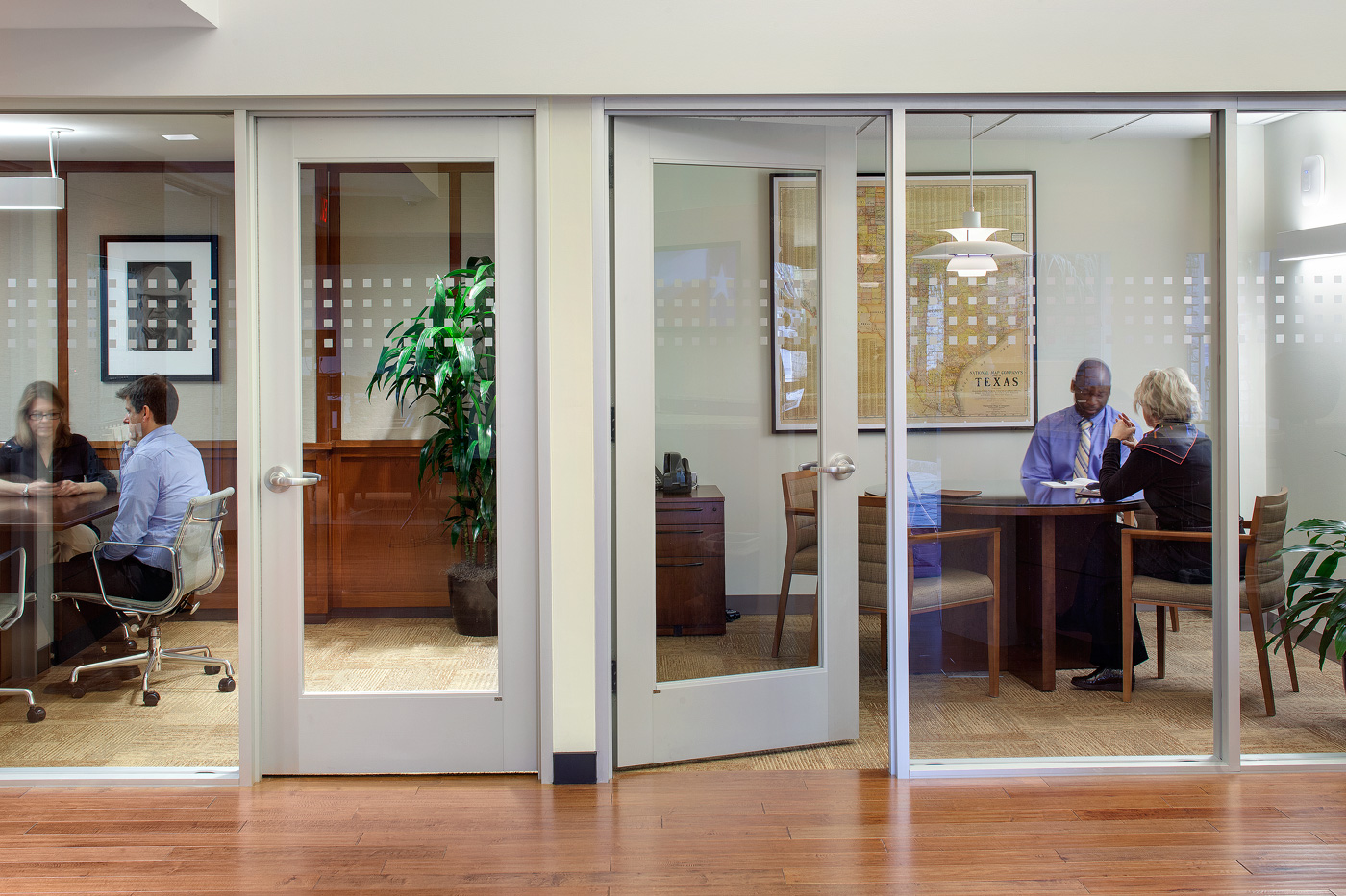 People meeting in neighboring glass conference rooms.