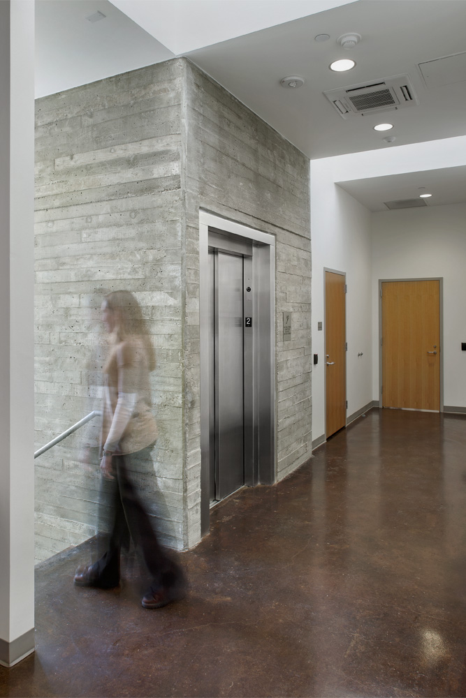 An exposed concrete elevator shaft neighboring a staircase.