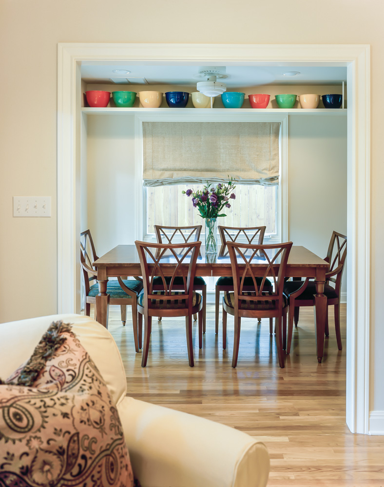 A dining table with flowers in vase in center.