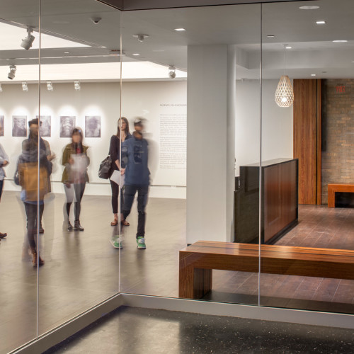 People in art exhibit visible through large glass wall.