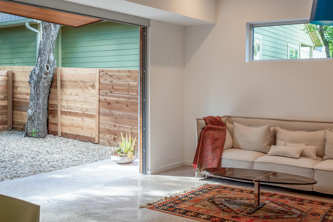 A couch and coffee table inside connected directly to a backyard through a large garage door sized opening in a wall.