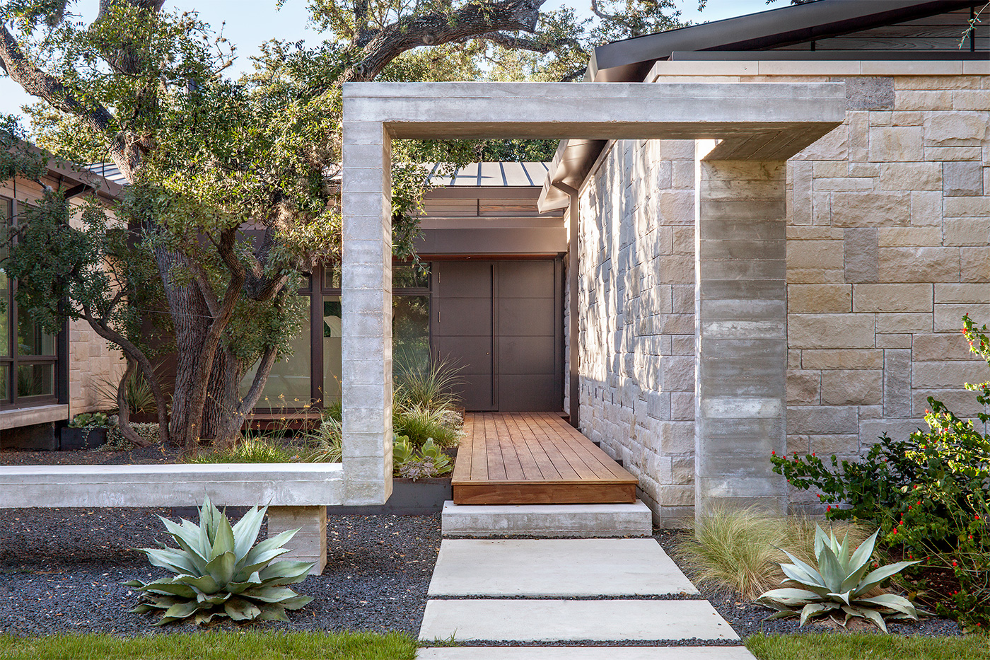 A path to the front entrance of a home passing under a geometric concrete arch.