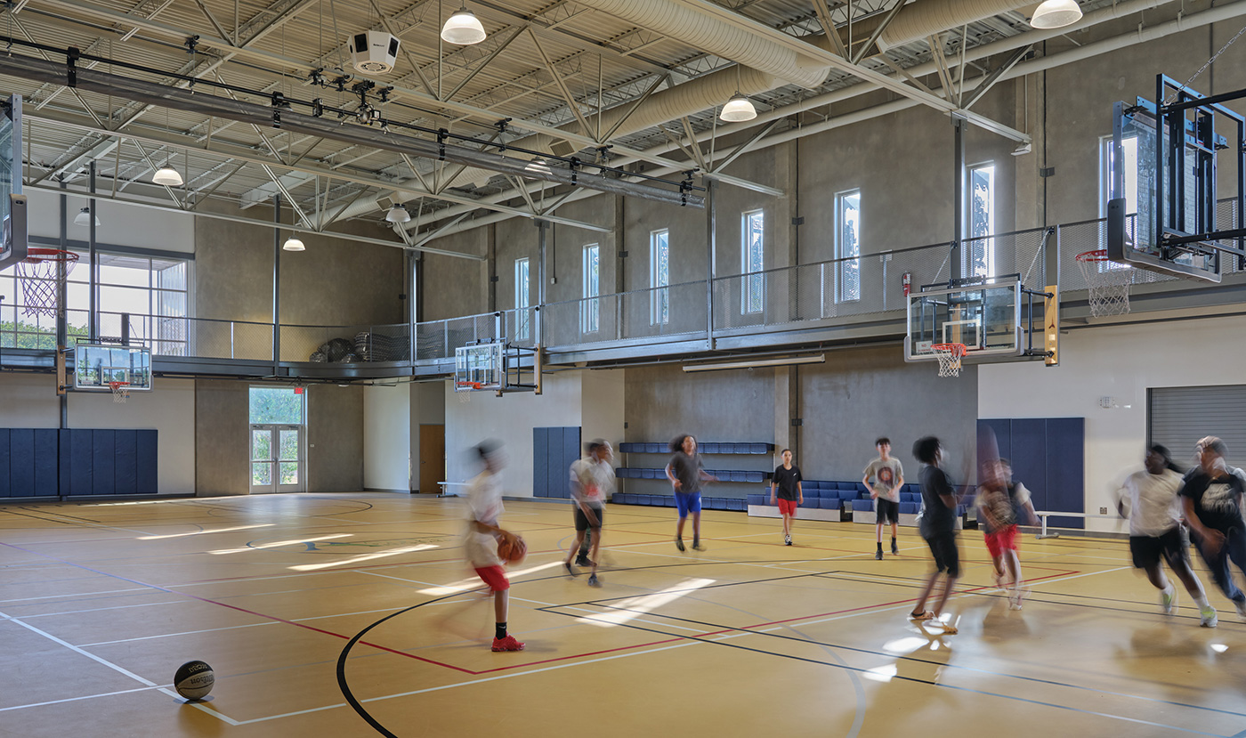 Many children playing basketball on an indoor court.