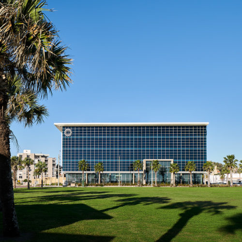 A view of a mostly glass office building from the beach it faces.