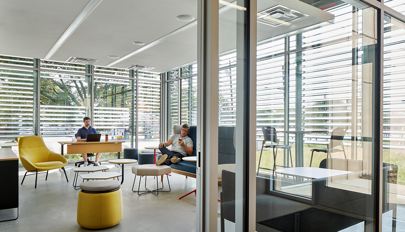 People working in communal sitting area with floor to ceiling windows.