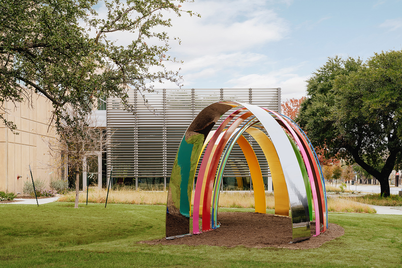 A colorful large sculpture in grass outside of a building.
