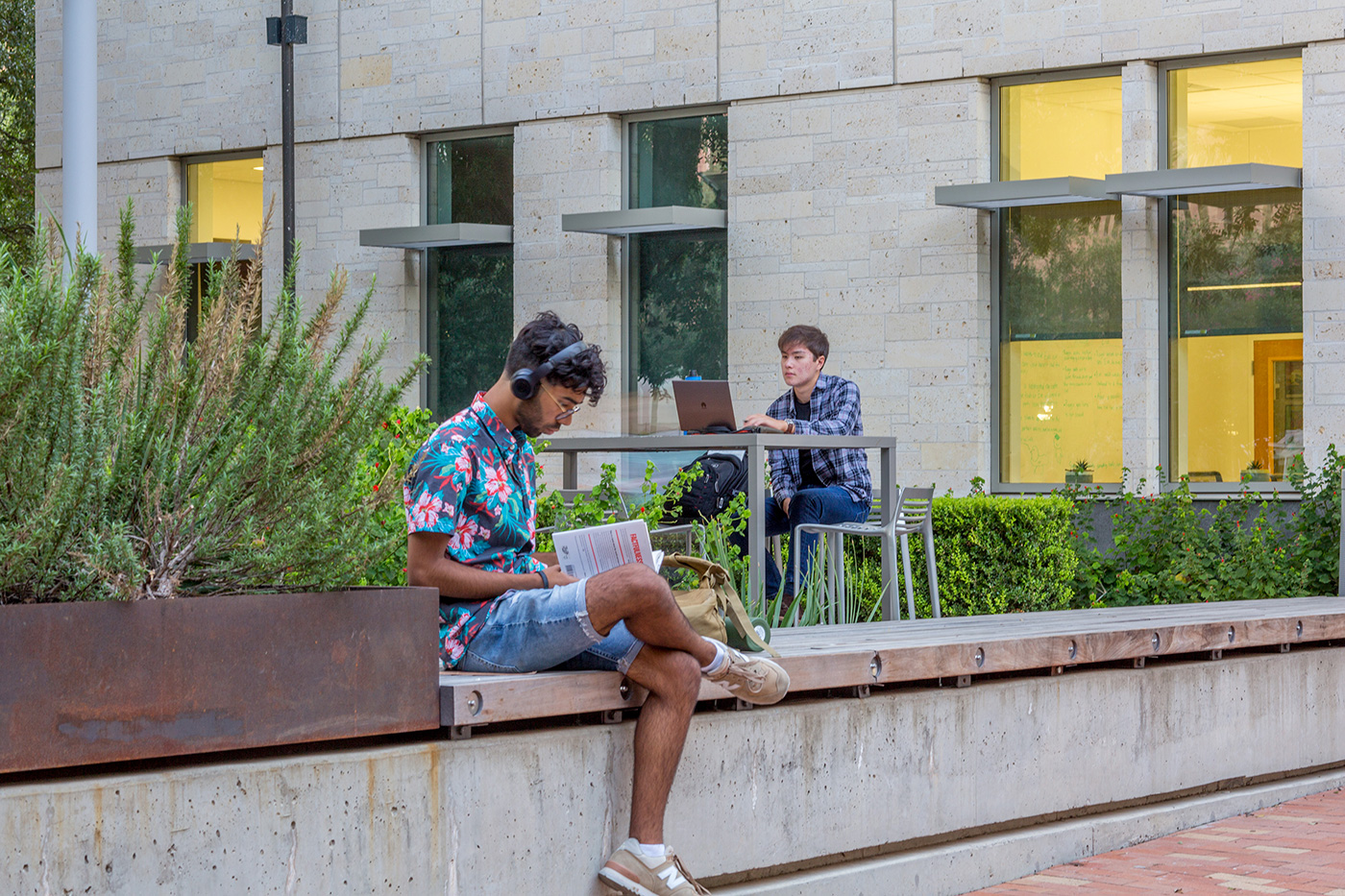 Man reading book with sitting on large curb feature.