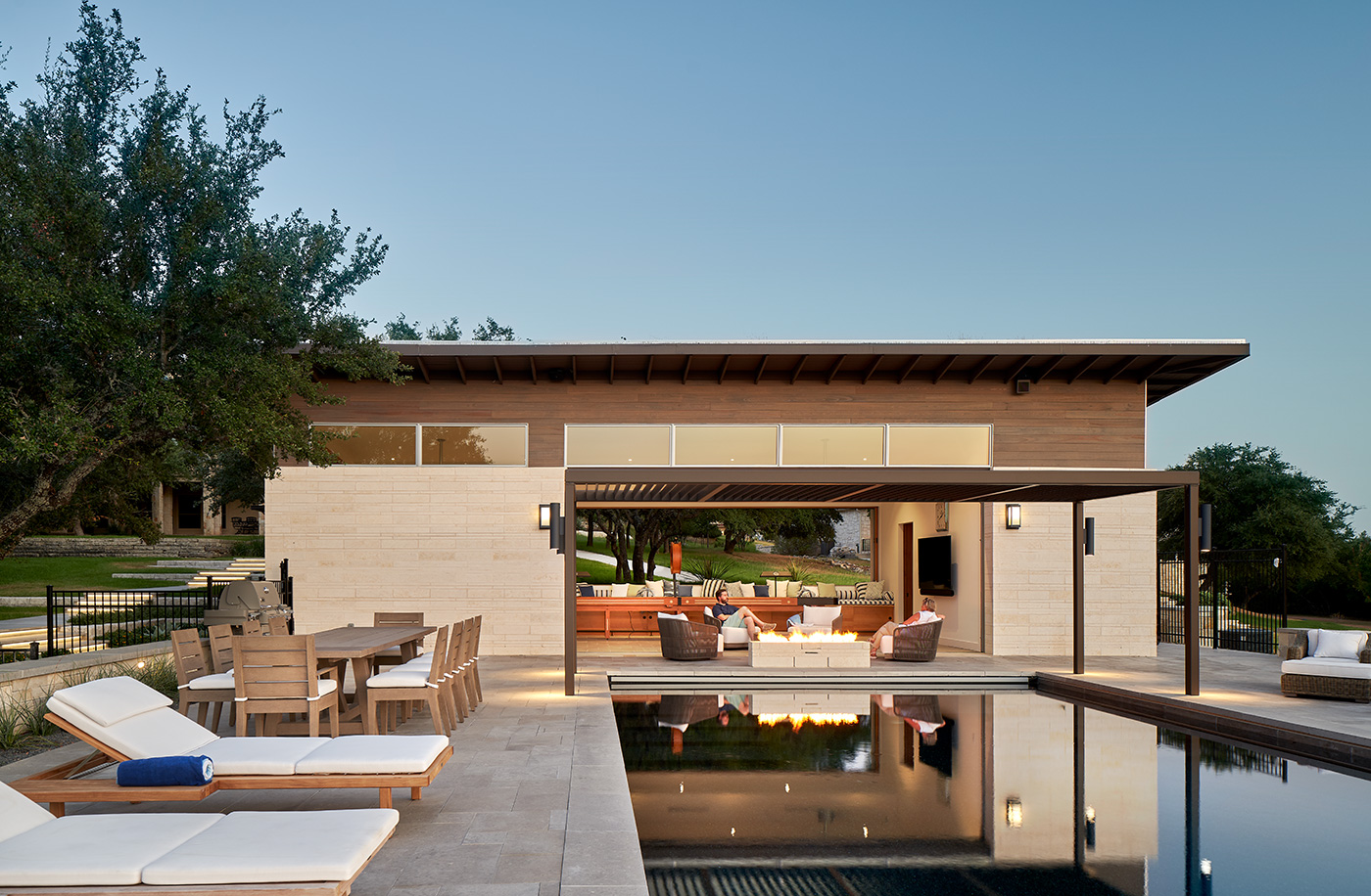 People sitting at outdoor fire pit next to pool at dusk.