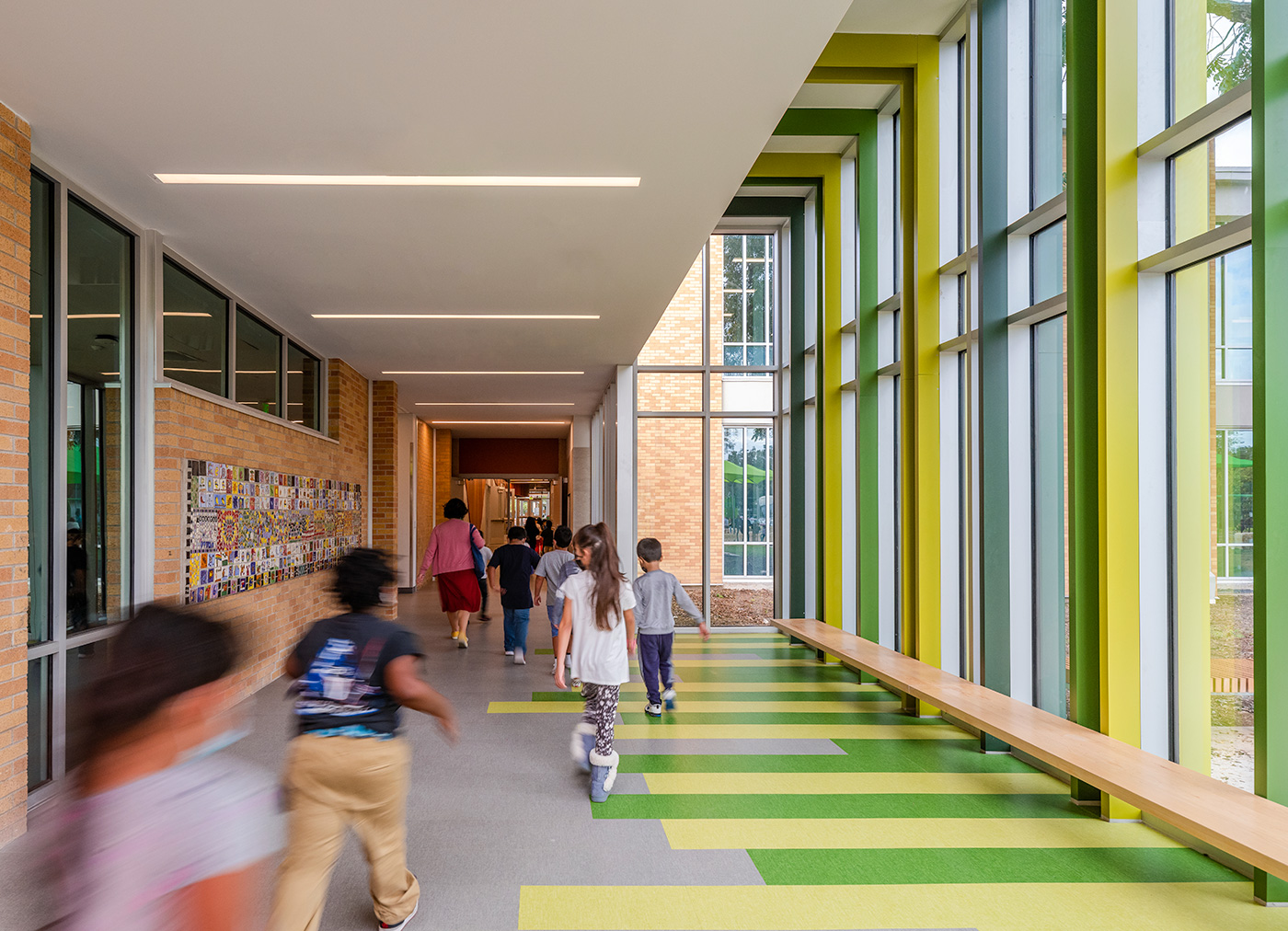 Kids walking past large windows of a hallway in a line.