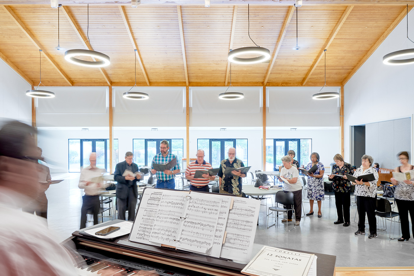 People singing from books in front of man at piano.