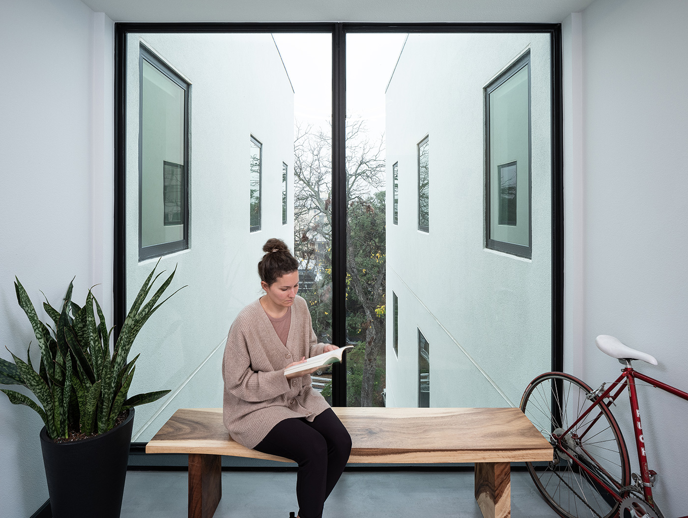 women reading at on wooden bench in front of large window.