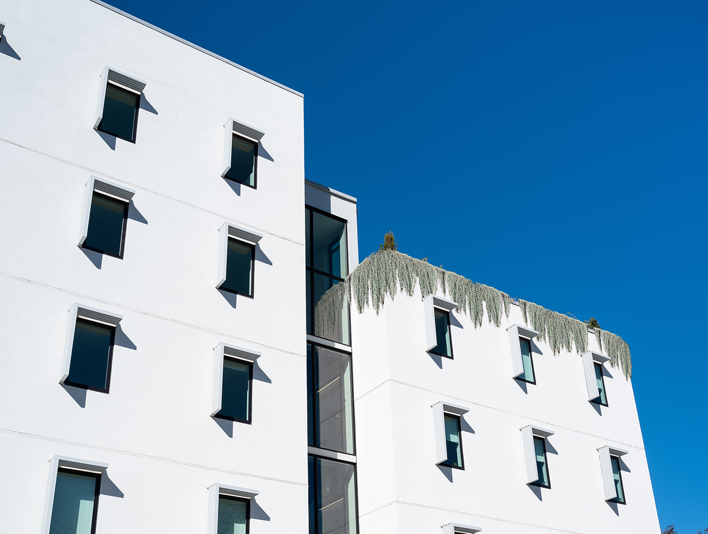 facade of white apartment building with plants hanging down from roof.