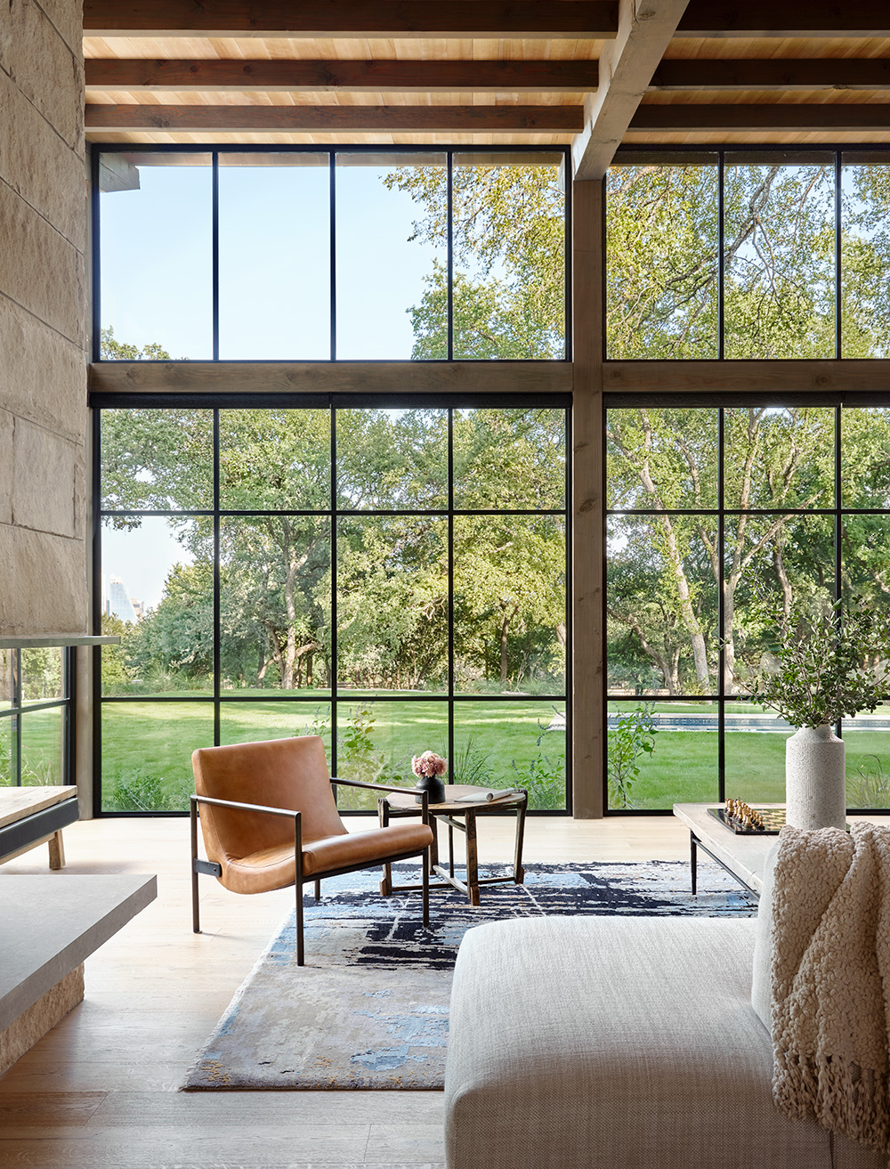 A modern furnished living room positioned in front of large windows that look out to a backyard.