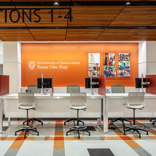 A row of desks in front a wall the reads " The University of Texas at Austin Texas One Stop".