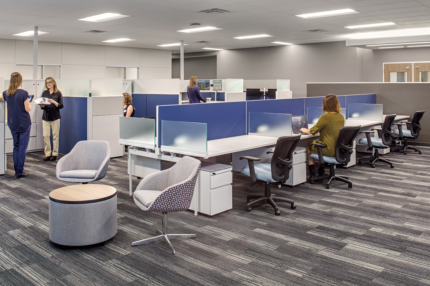 People work at and stand around desks in a office.