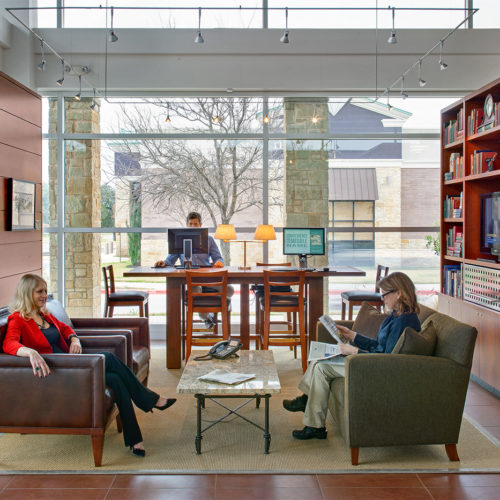 People sitting in a lobby setting featuring a bookshelf and couches.