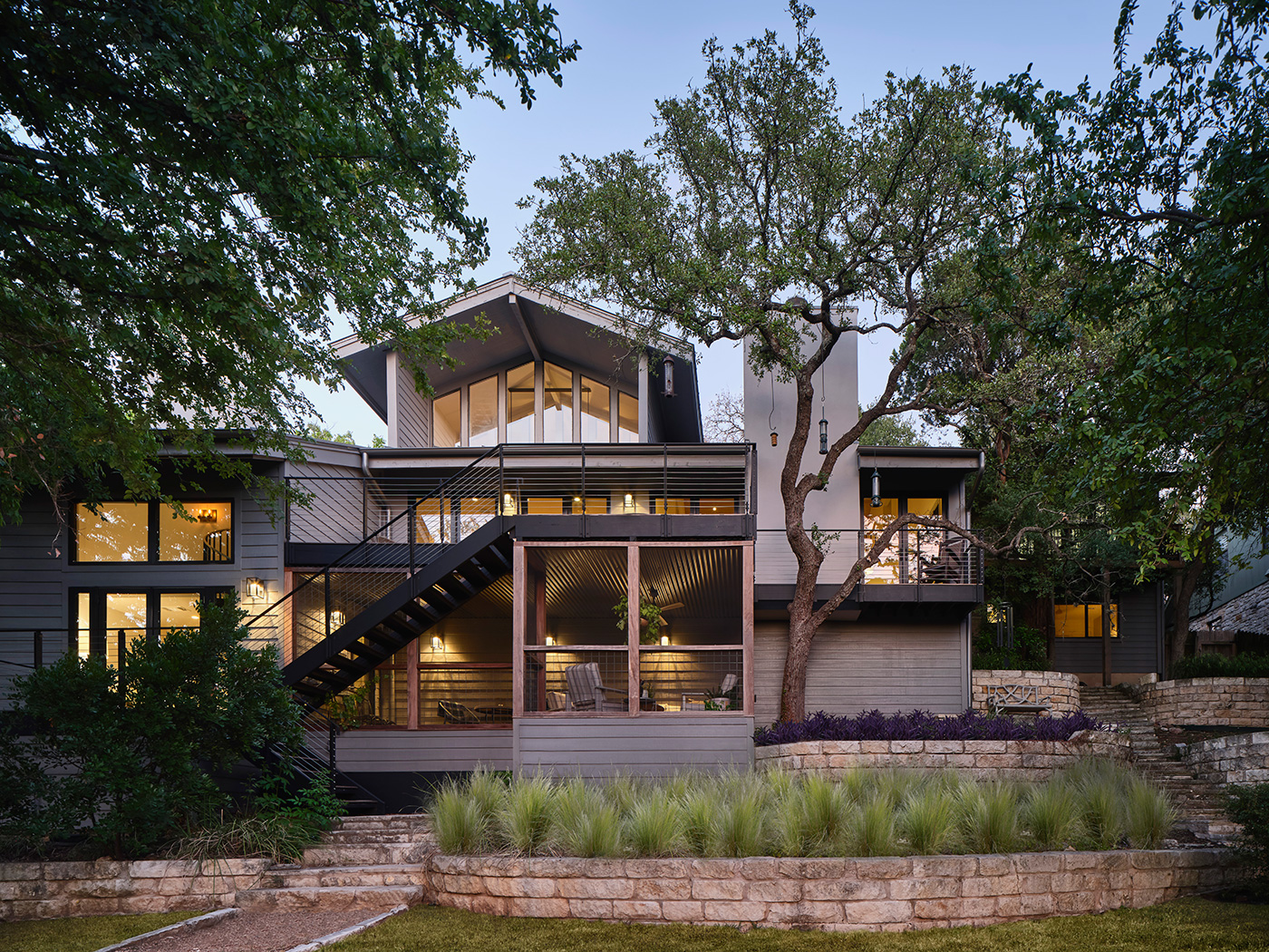 View of a three-story house from its backyard surrounded by diverse landscaping.