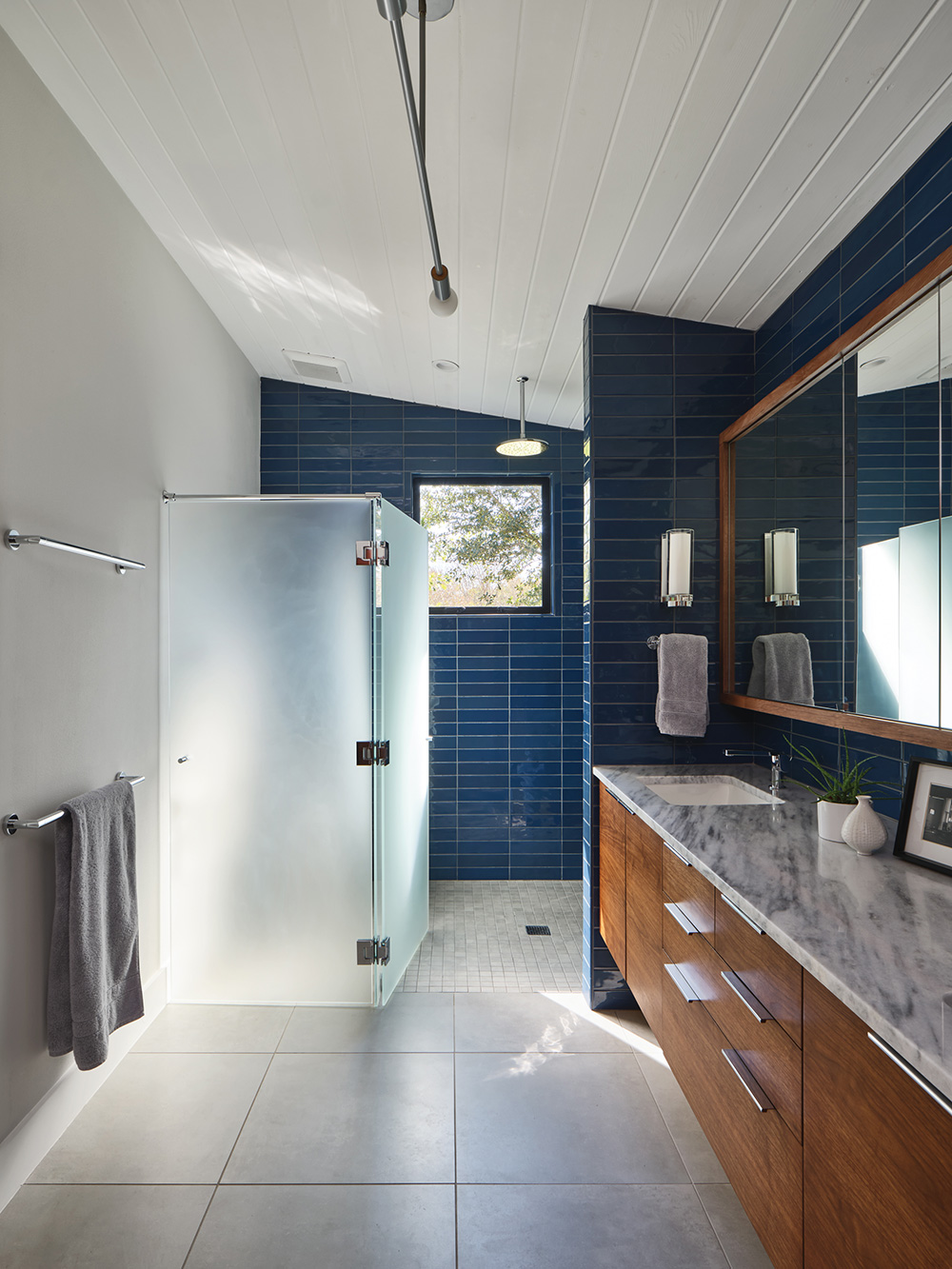 Opaque glass shower soor with blue tiled wall in bathroom.