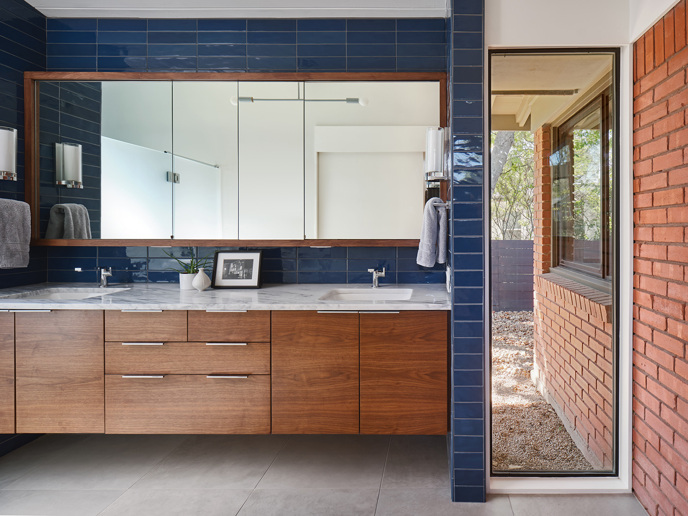 His and her sink with dark wood cabinets and blue tile on walls.