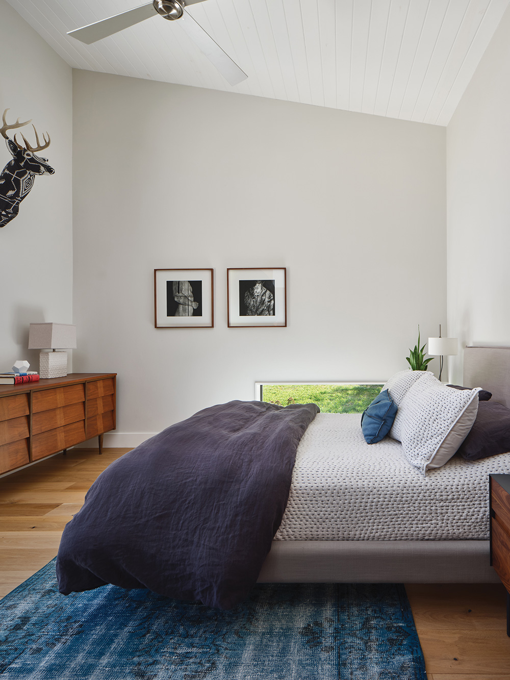 A large bed in a white modern room with e a slanted ceiling.