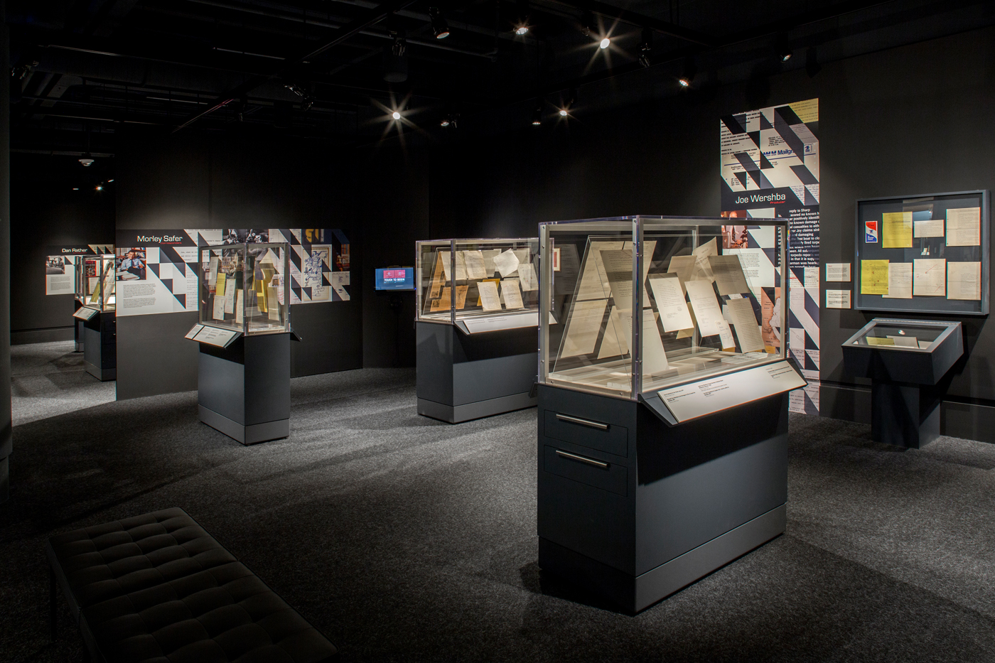 Dark exhibit room with display cases displaying many documents.