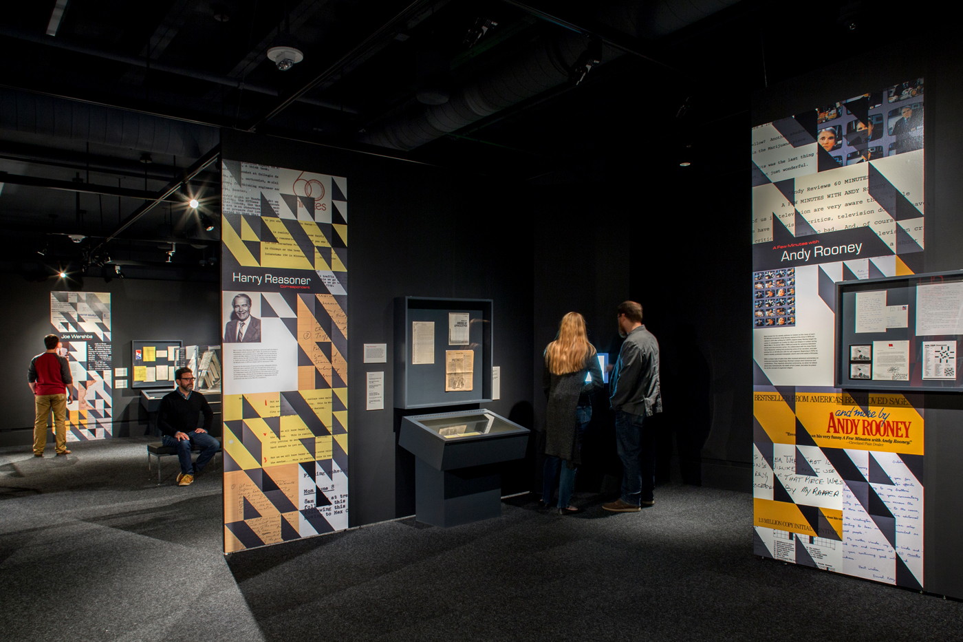 People standing and sitting around a dim intimate exhibit.