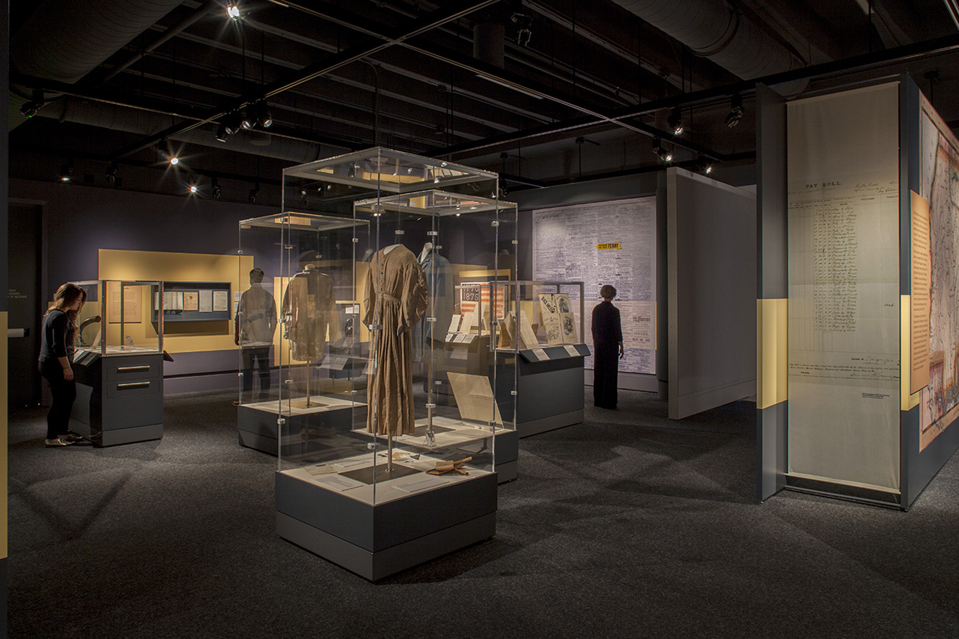 Large dim exhibit room with three display cases showing historic attire.