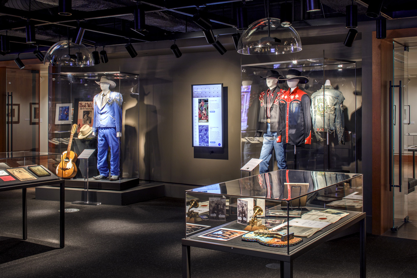 outfits and objects contained in display cases lit in dim exhibit room.