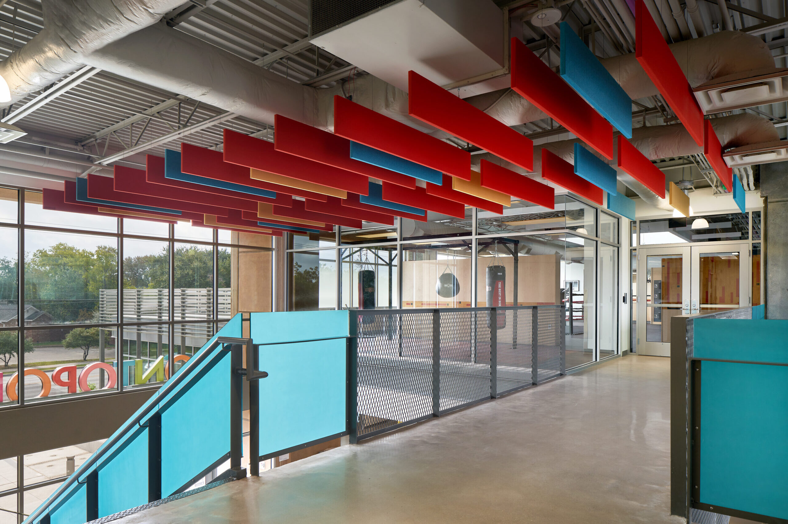 upstairs lobby with view of railings in foreground, building's front windows to the left, and exercise room with boxing punching bags to the right