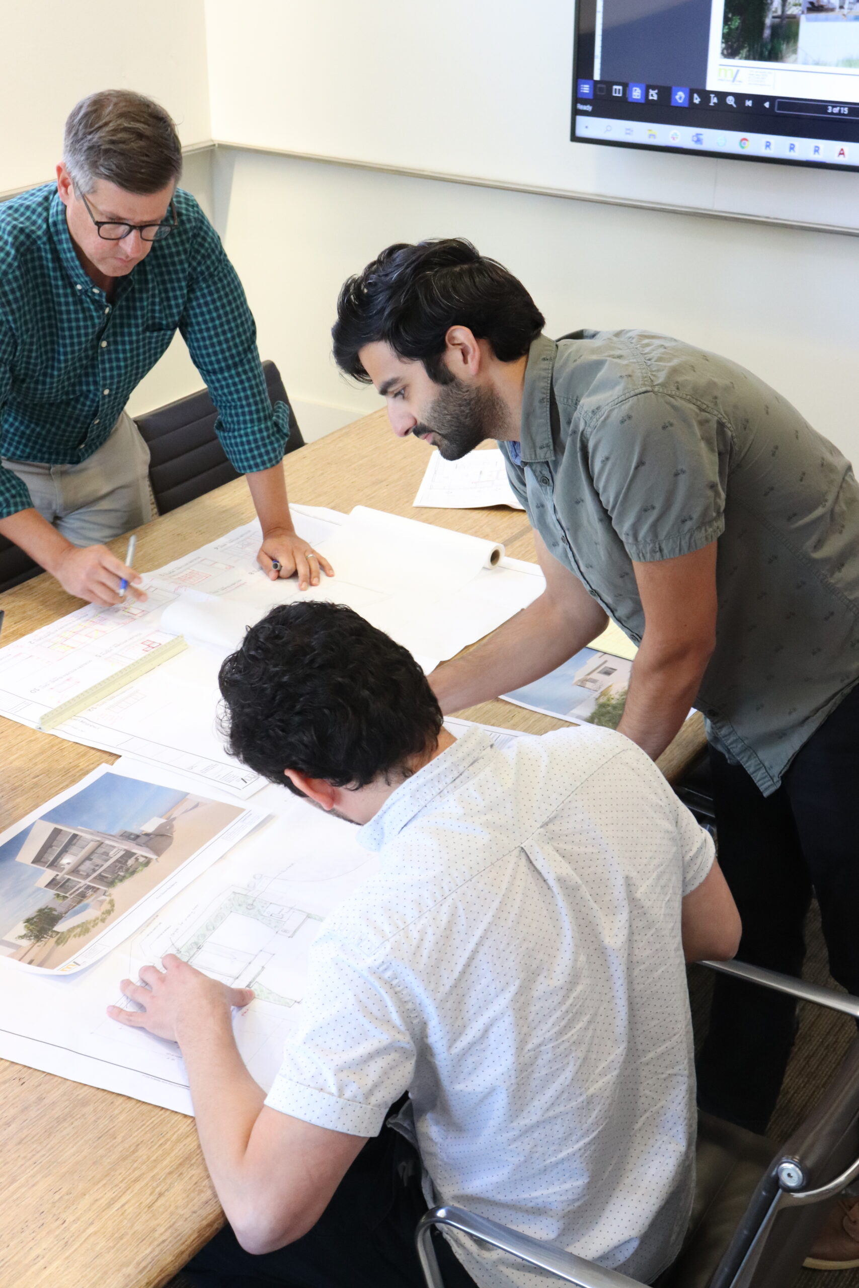 staff gathered around conference table reviewing construction drawings and project renderings