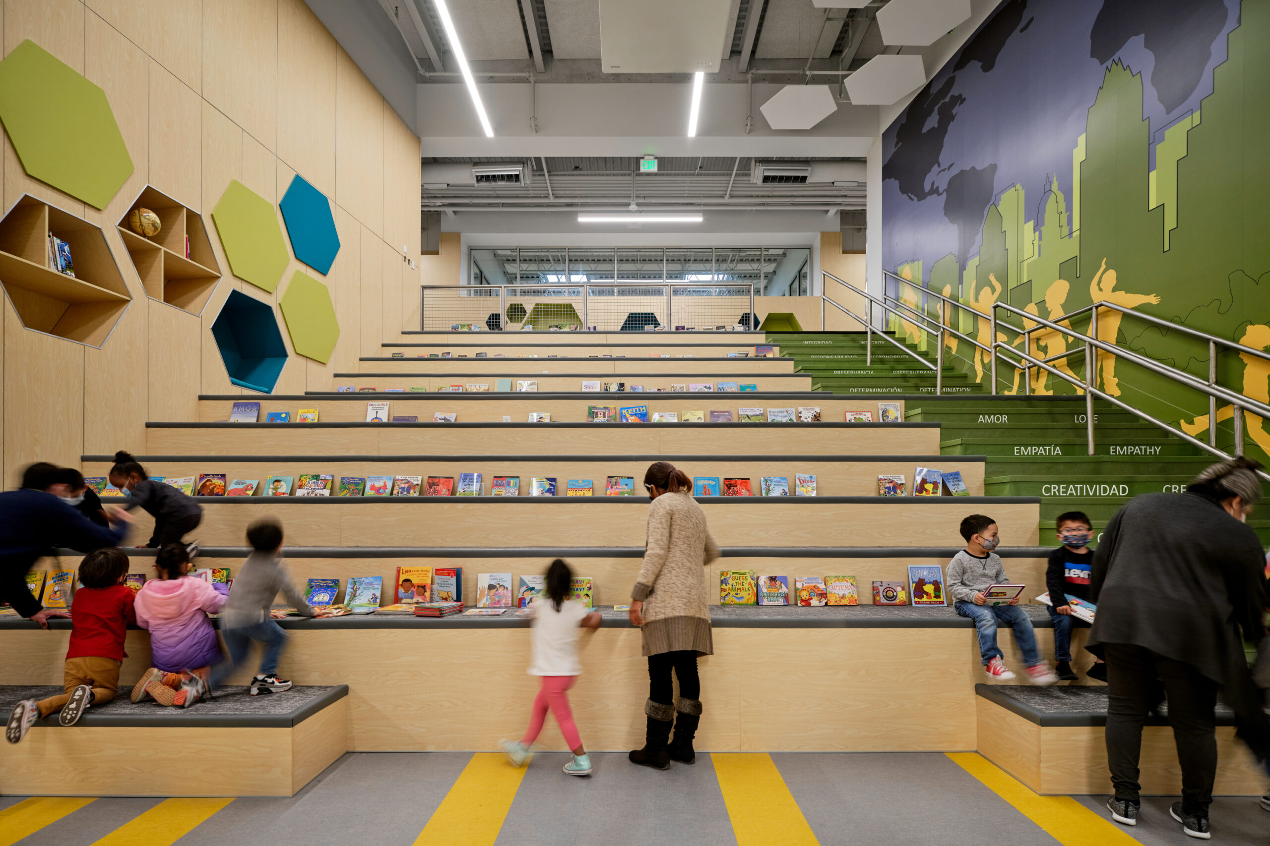 straight on view of stairway that also functions as a social gathering space in elementary school, books are displayed on the levels and children and teachers are in the foreground