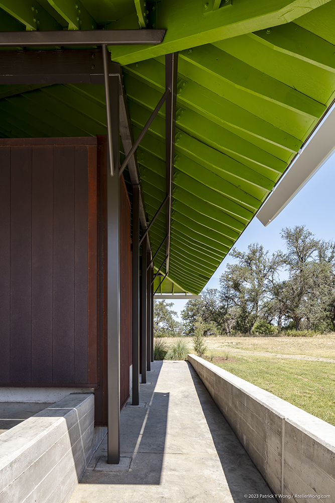 View of the underside of a roof painted green above weathered steel walls.