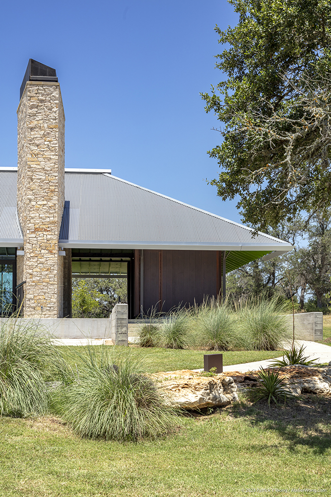 Grass landscaping in front of a building with tall stone chimney.