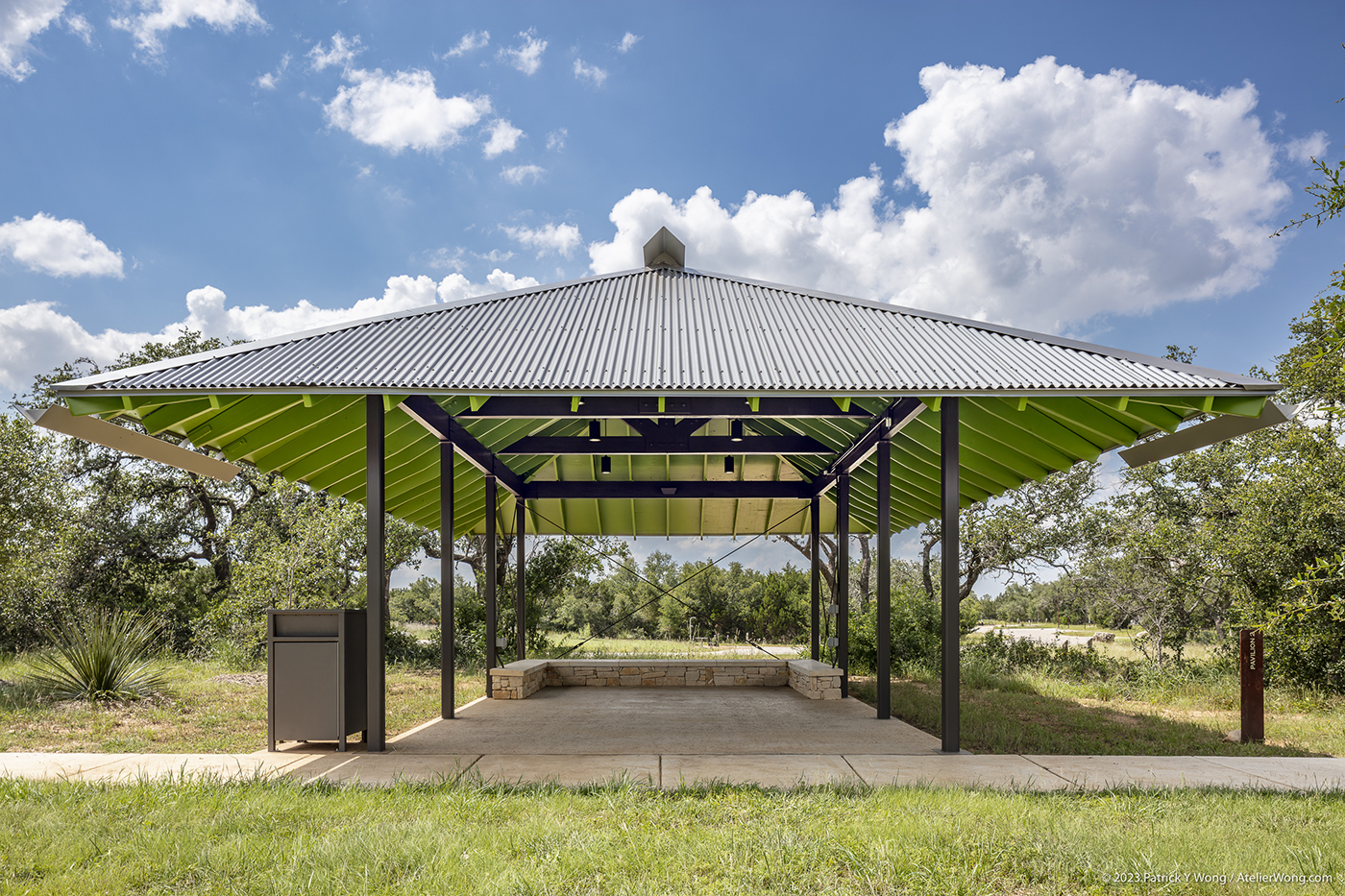 A covered outdoor pavilion with a U-shaped stone bench.