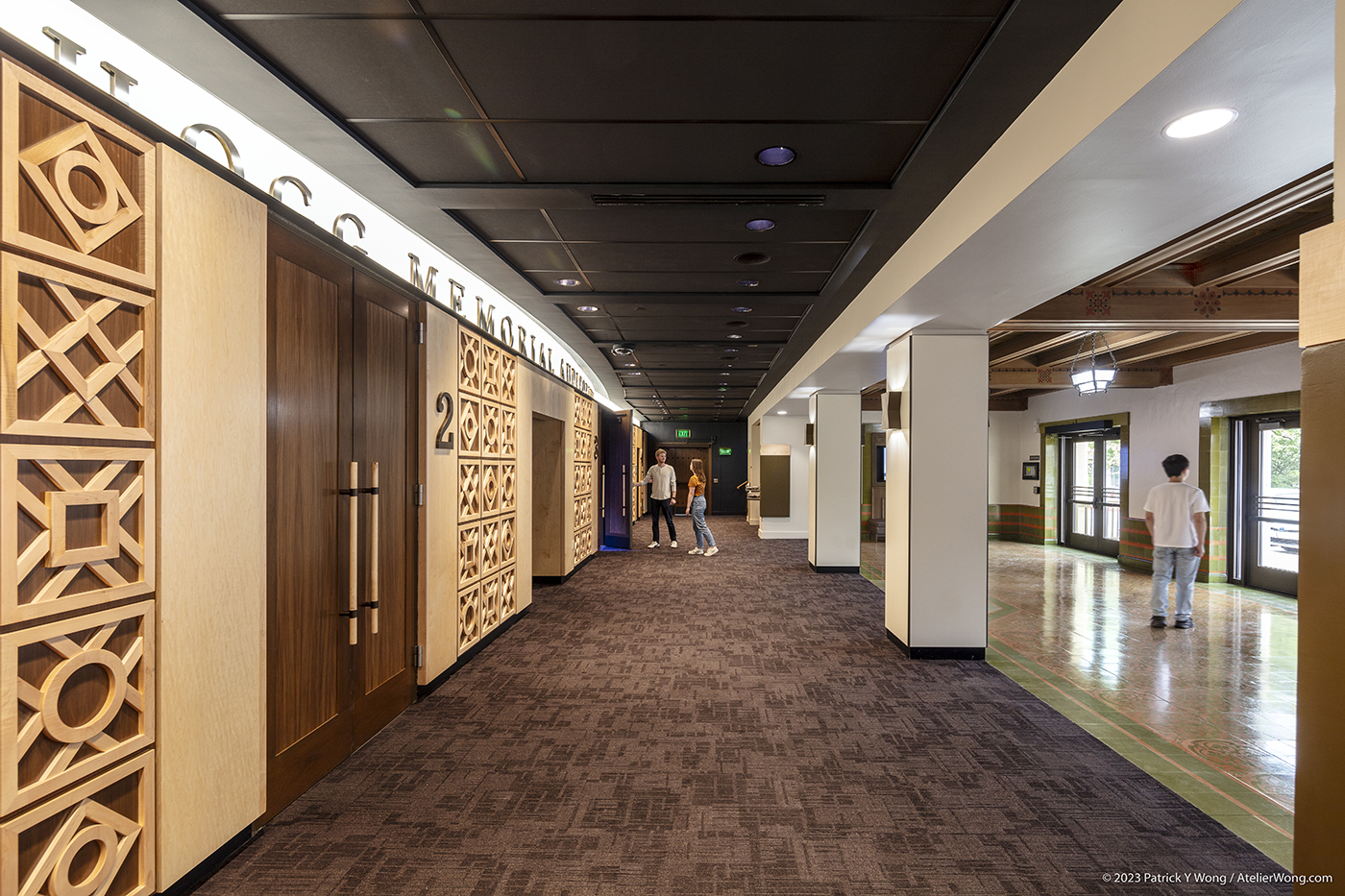 People walking through a lobby with a decorative wood wall.