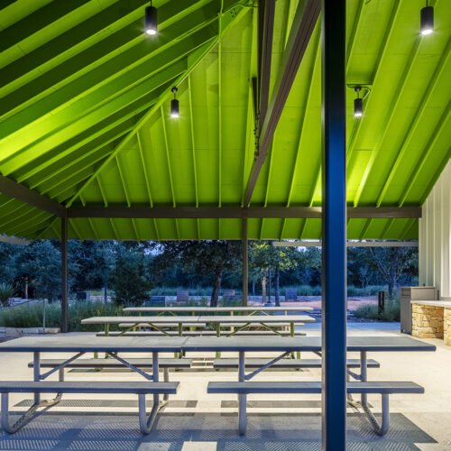 Outdoor picnic tables under a brightly lit roof at dusk.