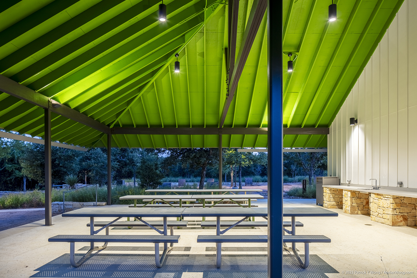 Outdoor picnic tables under a brightly lit roof at dusk.