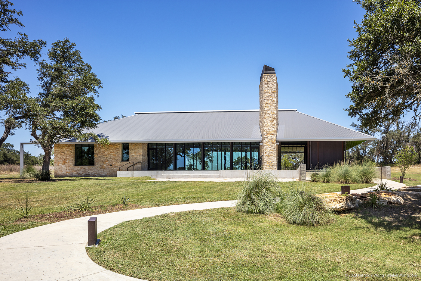 A concrete path leading to a building with a slanted metal roof and a tall stone chimney.